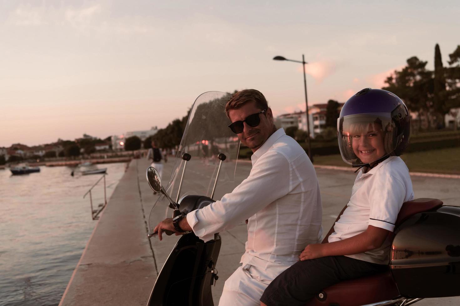 en far med hans son åtnjuter en semester ridning en skoter förbi de hav i de tidigt morgon. selektiv fokus foto