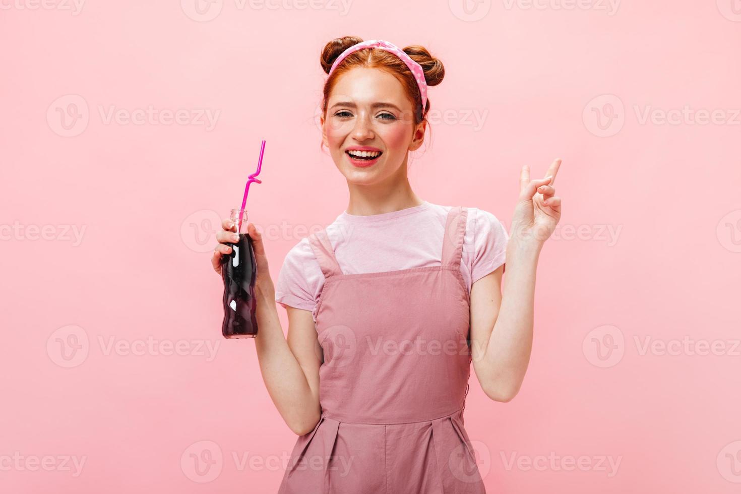 full längd skott av eleganta ung kvinna i rosa overall dricka ljuv soda på isolerat bakgrund foto