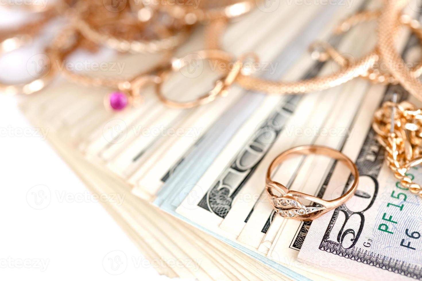 många dyr gyllene jewerly ringar, örhängen och halsband med stor belopp av oss dollar räkningar på vit bakgrund. pantbank eller jewerly affär foto