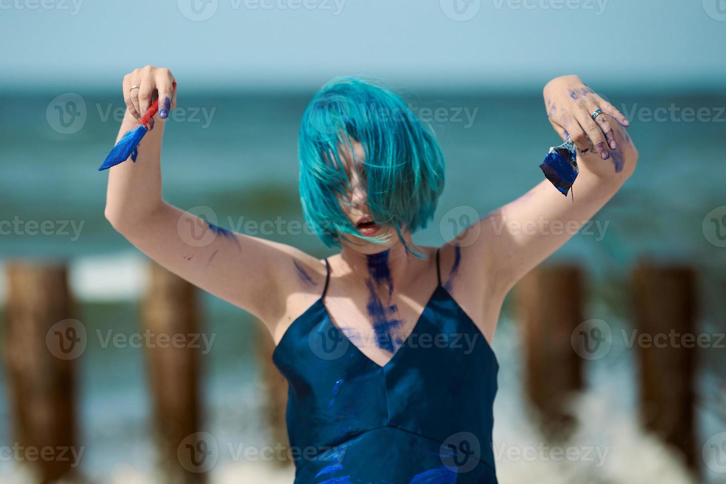 konstnärlig blåhårig kvinna performance artist insmord med blå gouache färger dans på stranden foto