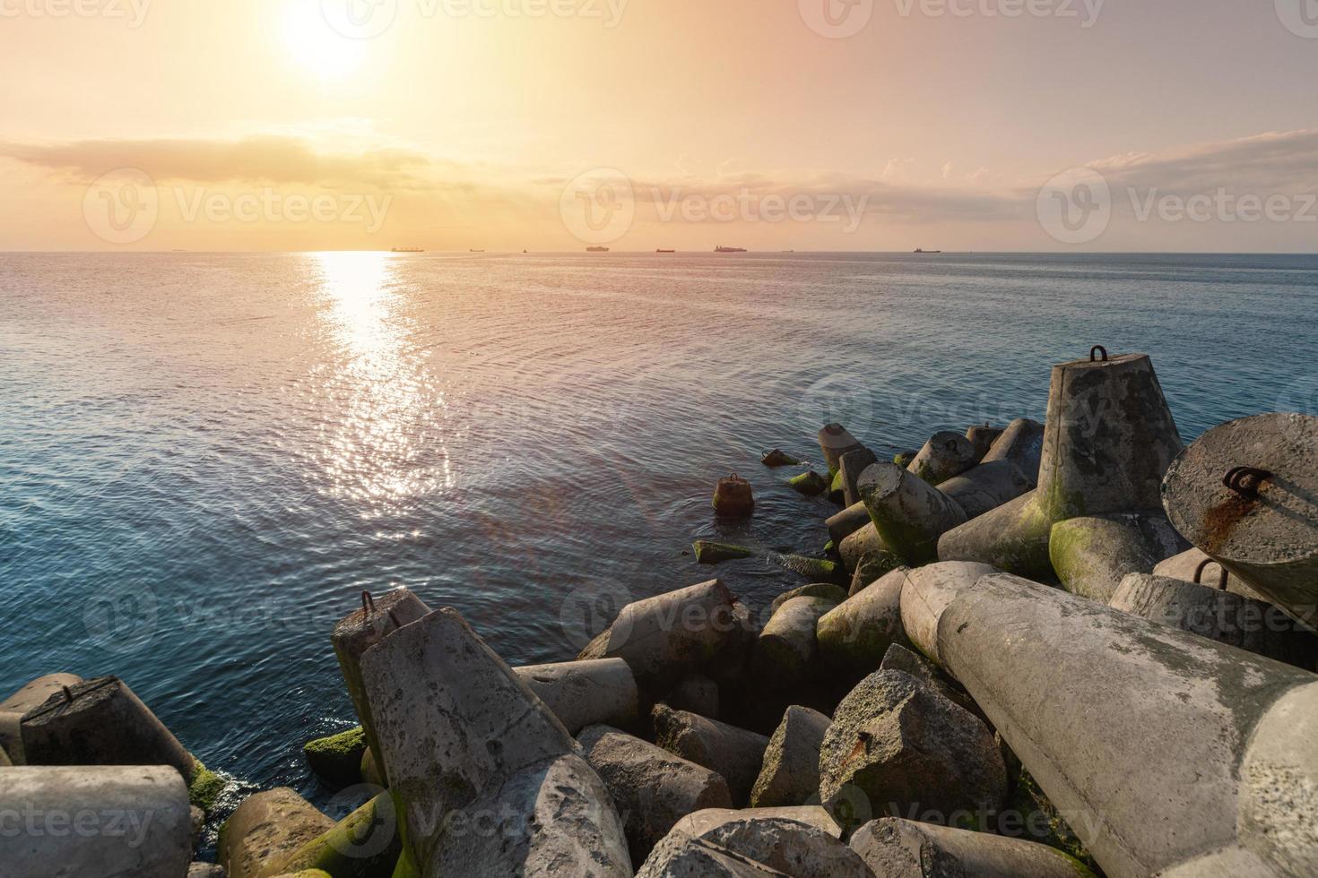 vacker solnedgång havslandskap. vågbrytare tetrapods i land vid piren. lastfartyg vid horisonten. resedrömmar och motivation foto