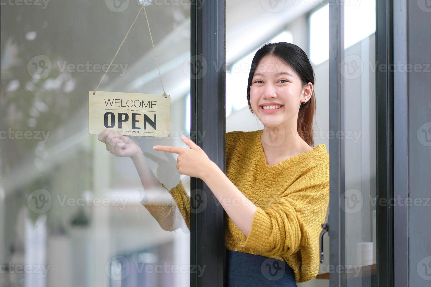 ung Asien chef flicka ändring en tecken från stängd till öppen tecken på dörr Kafé ser utanför väntar för klienter efter nedstängning. ägare små företag, mat och dryck, företag åter öppna om igen begrepp foto