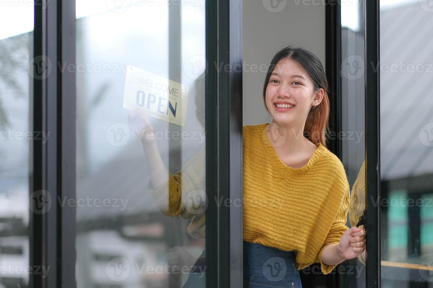 ung Asien chef flicka ändring en tecken från stängd till öppen tecken på dörr Kafé ser utanför väntar för klienter efter nedstängning. ägare små företag, mat och dryck, företag åter öppna om igen begrepp foto