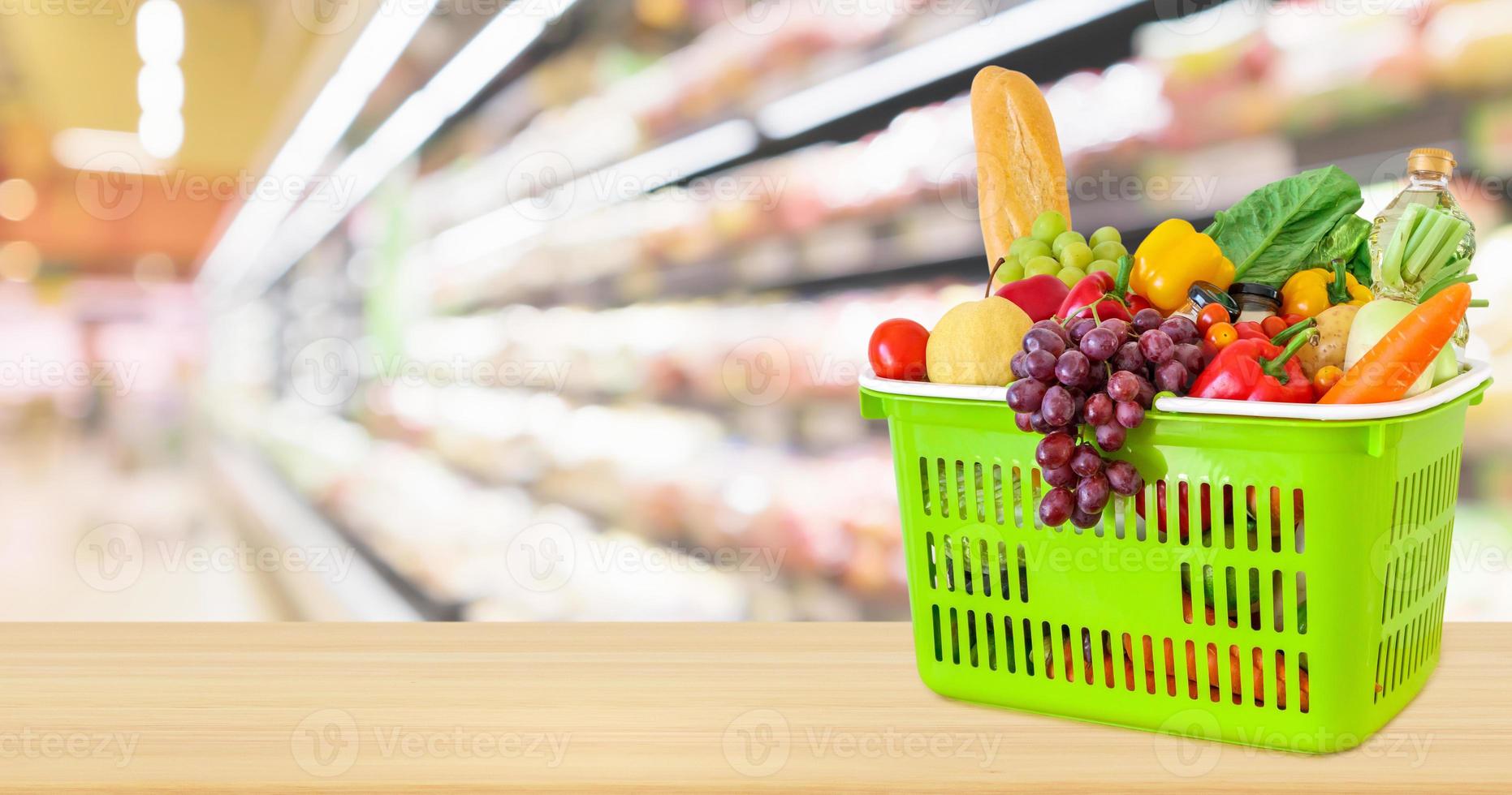 varukorg fylld med frukt och grönsaker på träbord med supermarket livsmedelsbutik suddig oskarp bakgrund med bokeh ljus foto