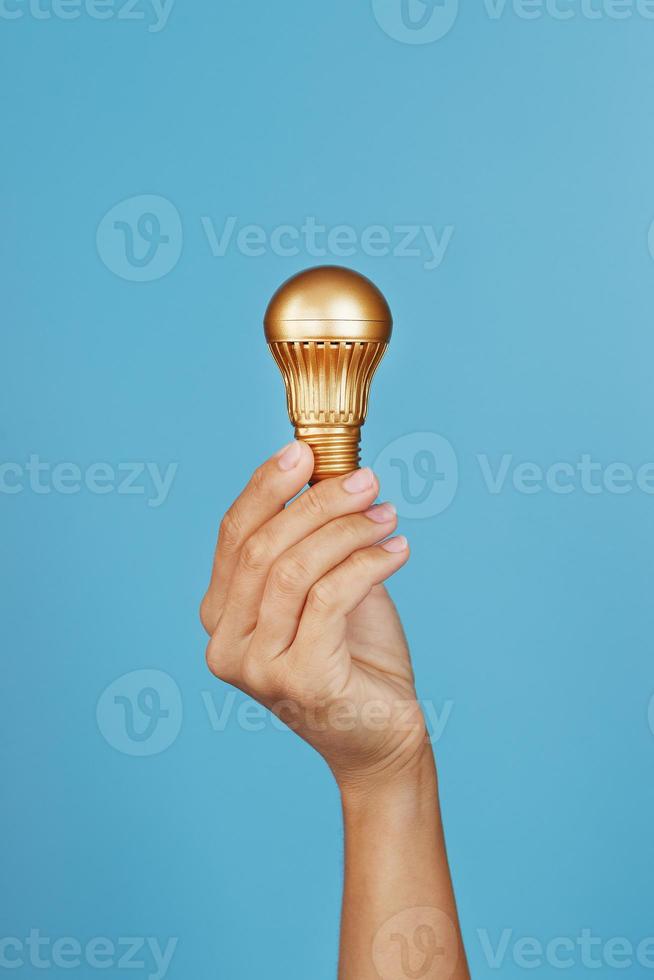 guld ljus Glödlampa i hand på en blå bakgrund, som en begrepp av idéer och bistånd foto