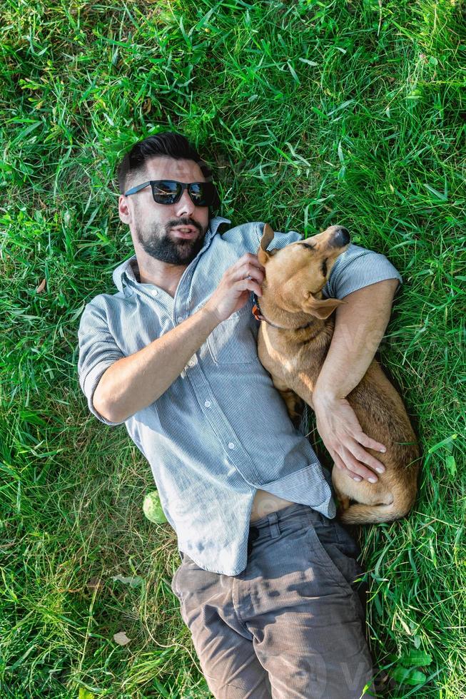 topp se av man och hund liggande på grön gräs. attraktiv europeisk man är kramas hans hund. foto