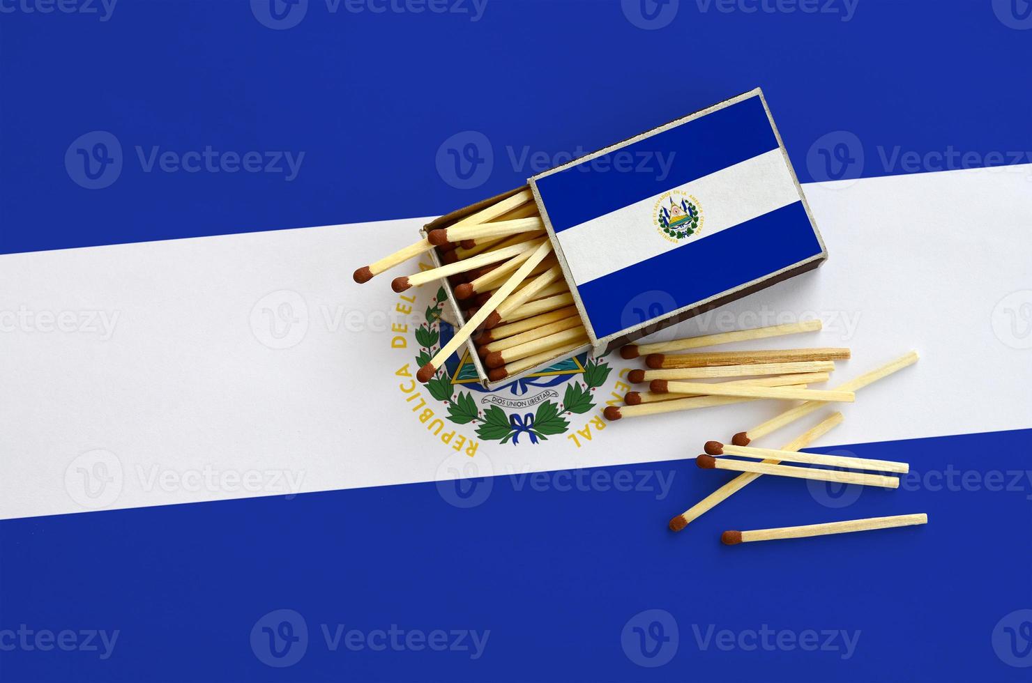 el salvador flagga är visad på ett öppen tändsticksask, från som flera tändstickor falla och lögner på en stor flagga foto