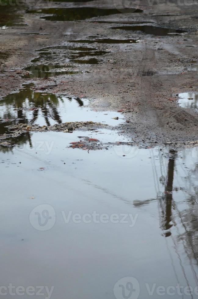 Foto av en fragment av en förstörd väg med stor vattenpölar i regnig väder