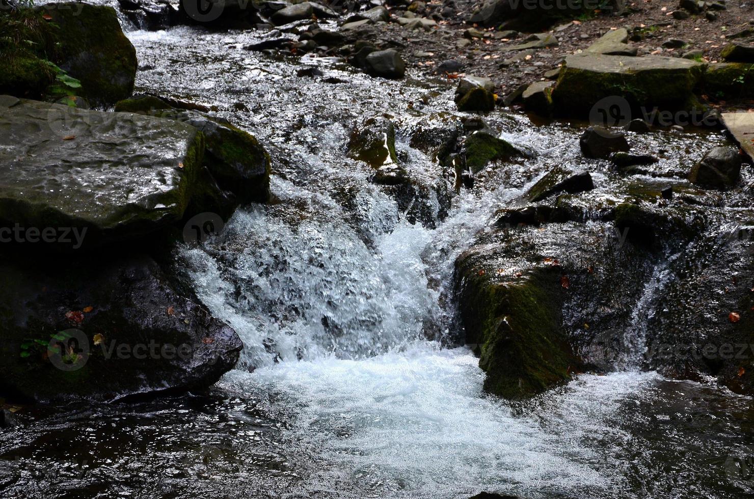 närbild bild av en små vild vattenfall i de form av kort strömmar av vatten mellan berg stenar foto