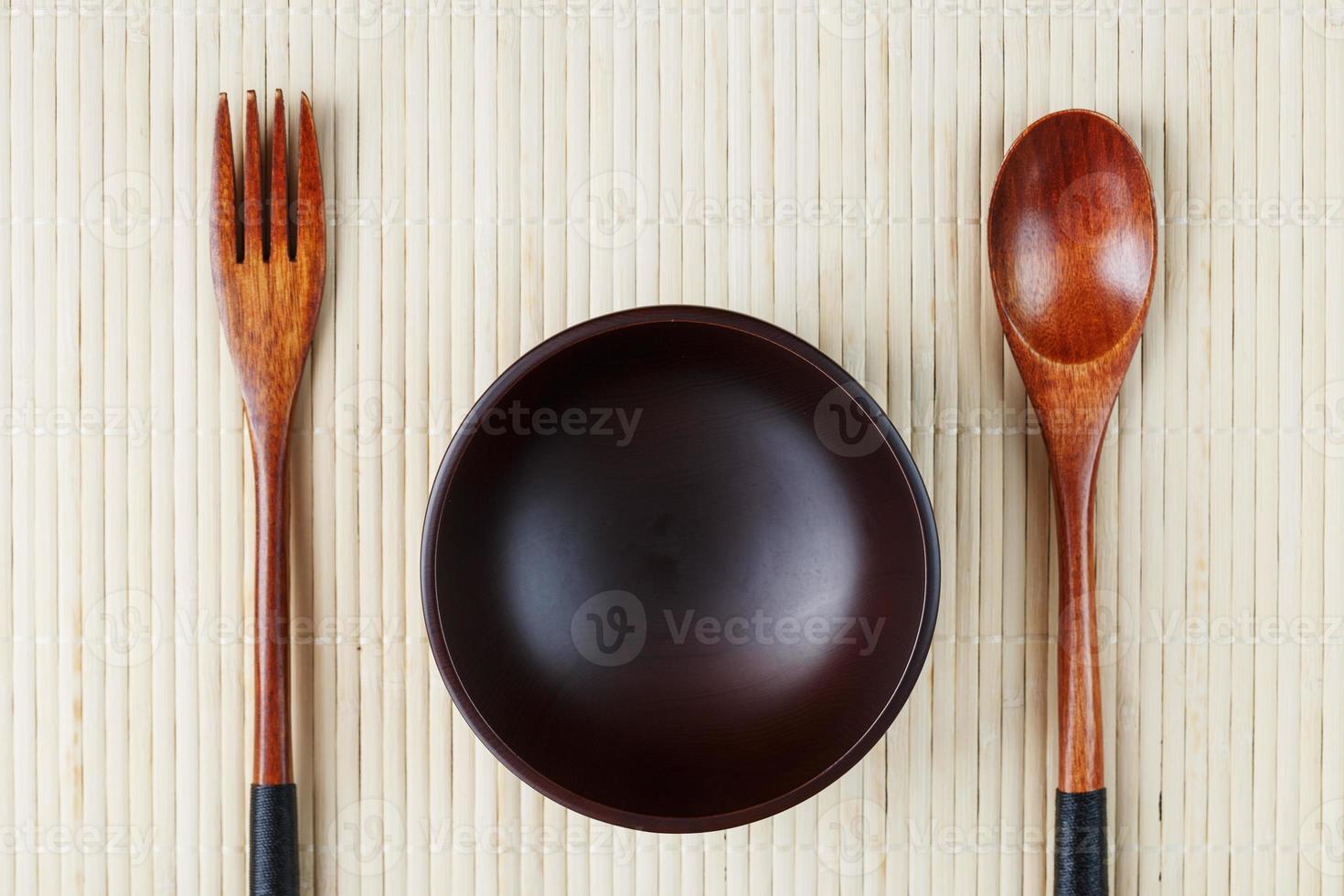 tömma mörk trä- kopp, sked och gaffel tillverkad av naturlig trä på en ljus bambu stöd foto