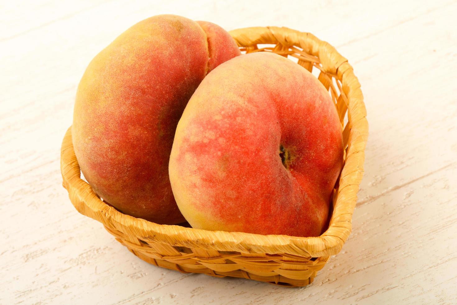ljuv persikor i en korg på trä- bakgrund foto