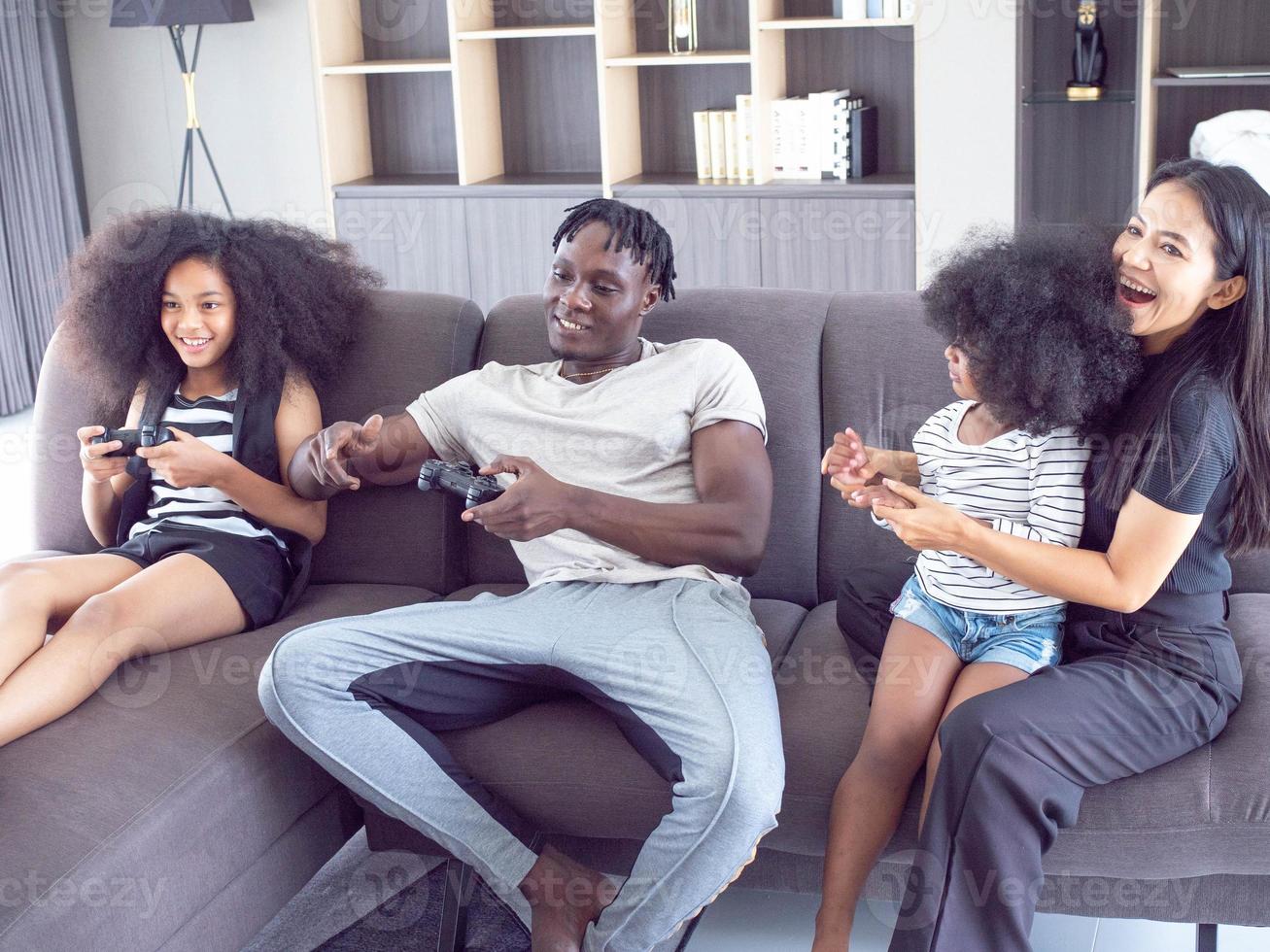 familj mor far son flicka afro svart afrika person Sammanträde soffa hobby spela video spel kontrollant joystick teknologi underhållning inomhus- levande rum Hem Lycklig leende livsstil foto