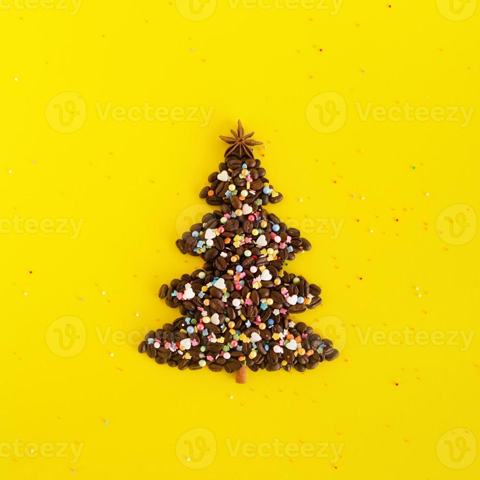 vinter- sammansättning med jul träd tillverkad förbi kaffe bönor och dekorerad anis stjärna, kanel pinne och flerfärgad kulinariska stänk på en gul bakgrund, platt lägga. hälsning kort för ny år. foto