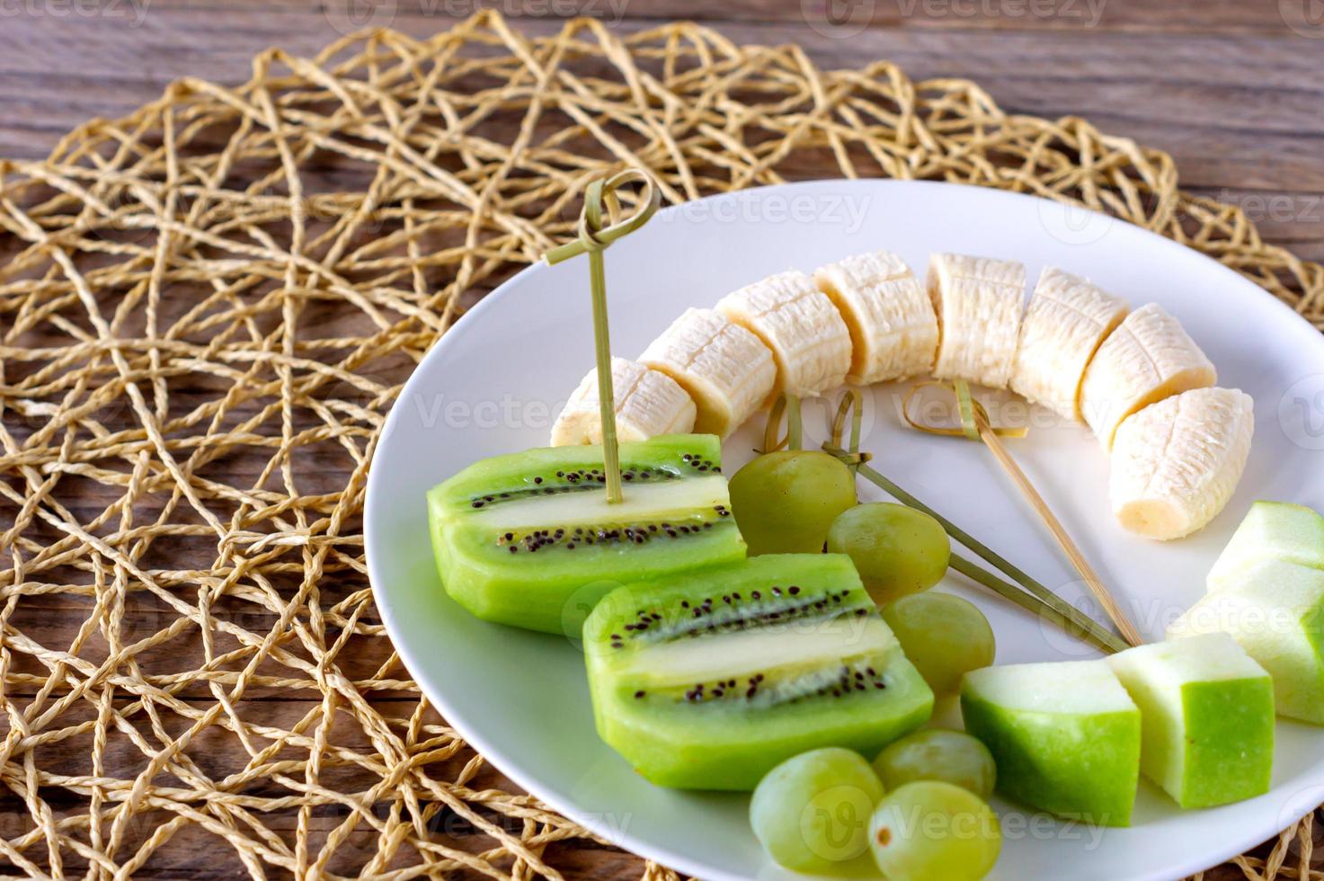 vegan frukost- mängd av frukter. äpplen, bananer, kiwi och vindruvor på en tallrik på de grå trä- tabell, selektiv fokus, frukt sallad foto