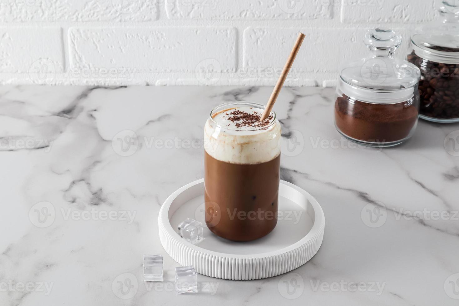 kall kaffe med mjölk, dalgona med is kuber på en vit bricka och marmor tabell. en underbar kyl- dryck i en varm dag. foto