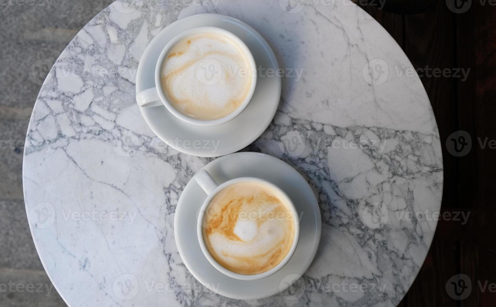 två koppar av cappuccino eller latte dekorerad med skum på marmor tabell bakgrund i kaffe affär. morgon- kaffe för par i kärlek. topp se. två vit muggar av kaffe. foto