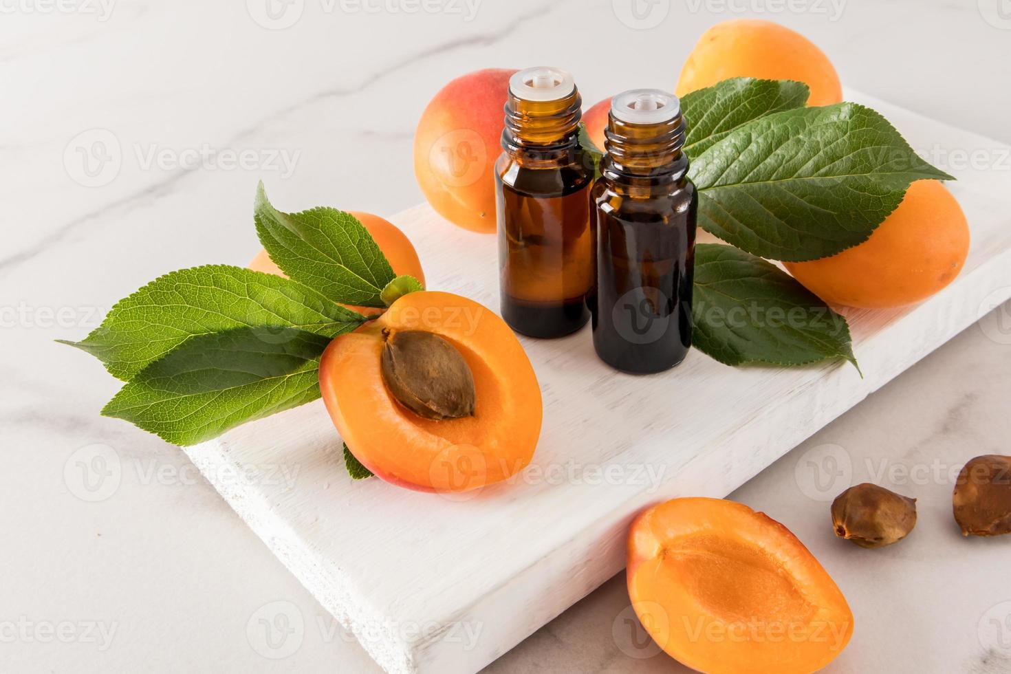 två medicinsk flaskor med en dropper med aprikos utsäde olja stå på en vit trä- podium bland mogen aprikoser. naturlig kosmetika. foto