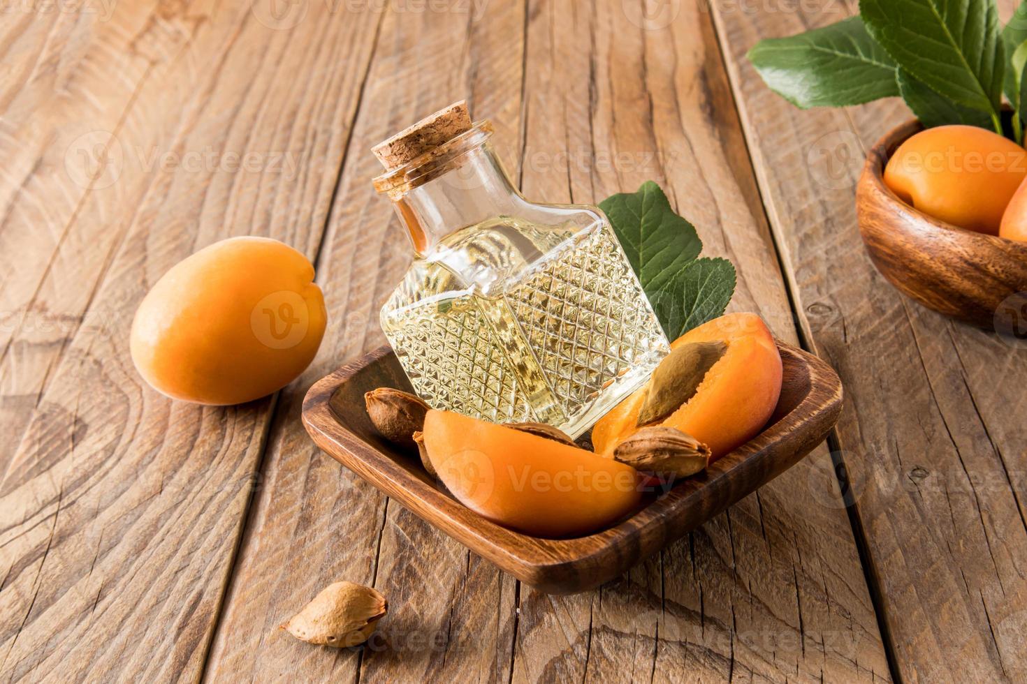 glas flaska med en kork lock med aprikos kärna olja lögn i en trä- skål med mogen aprikoser. antioxidant vård, föryngring. foto