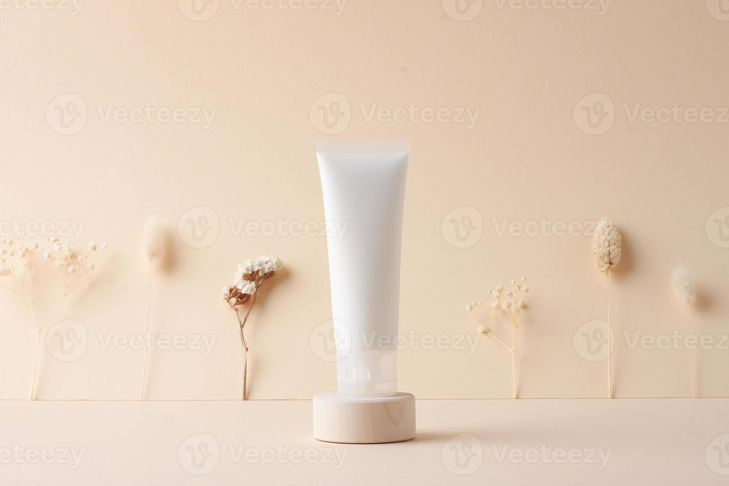 vit rör av kosmetisk grädde med blommor på trä- podium på beige bakgrund. stänga upp. foto