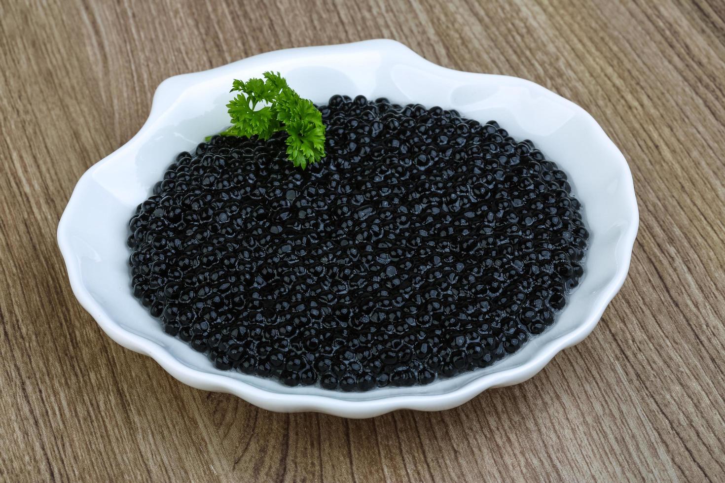 svart kaviar på tallriken och trä bakgrund foto