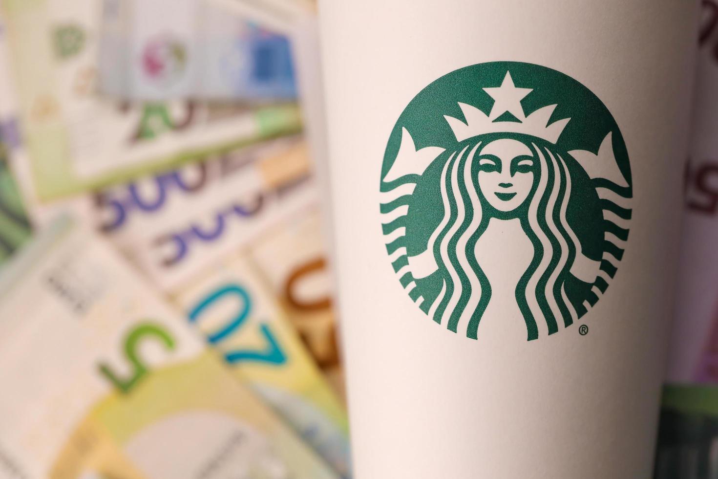 kharkiv, ukraina - december 16, 2021 vit papper kopp med starbucks logotyp och pengar räkningar. starbucks är de världens största kaffe hus med över 20 000 butiker. foto