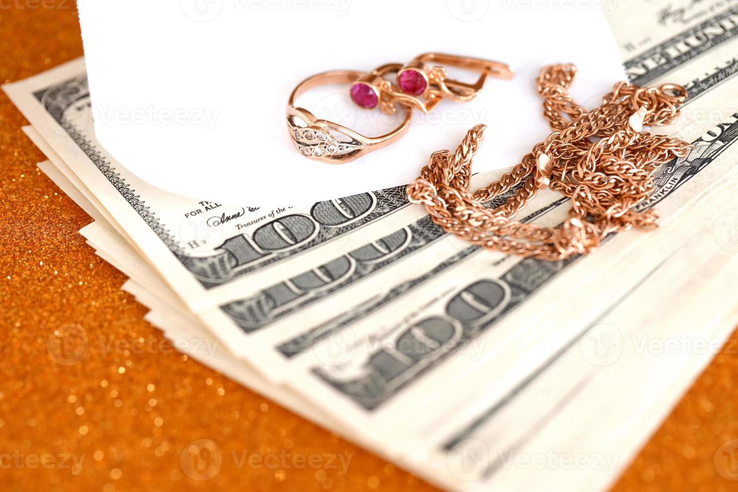 dyr gyllene jewerly ringa, örhängen och halsband med stor belopp av oss dollar räkningar på lyx glitter gyllene bakgrund yta. pantbank eller jewerly affär foto