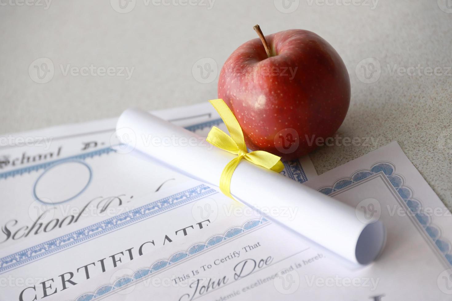 en hedra rulla erkännande, certifikat av prestation och hög skola diplom lögner på tabell med små skrolla och röd äpple. utbildning dokument foto