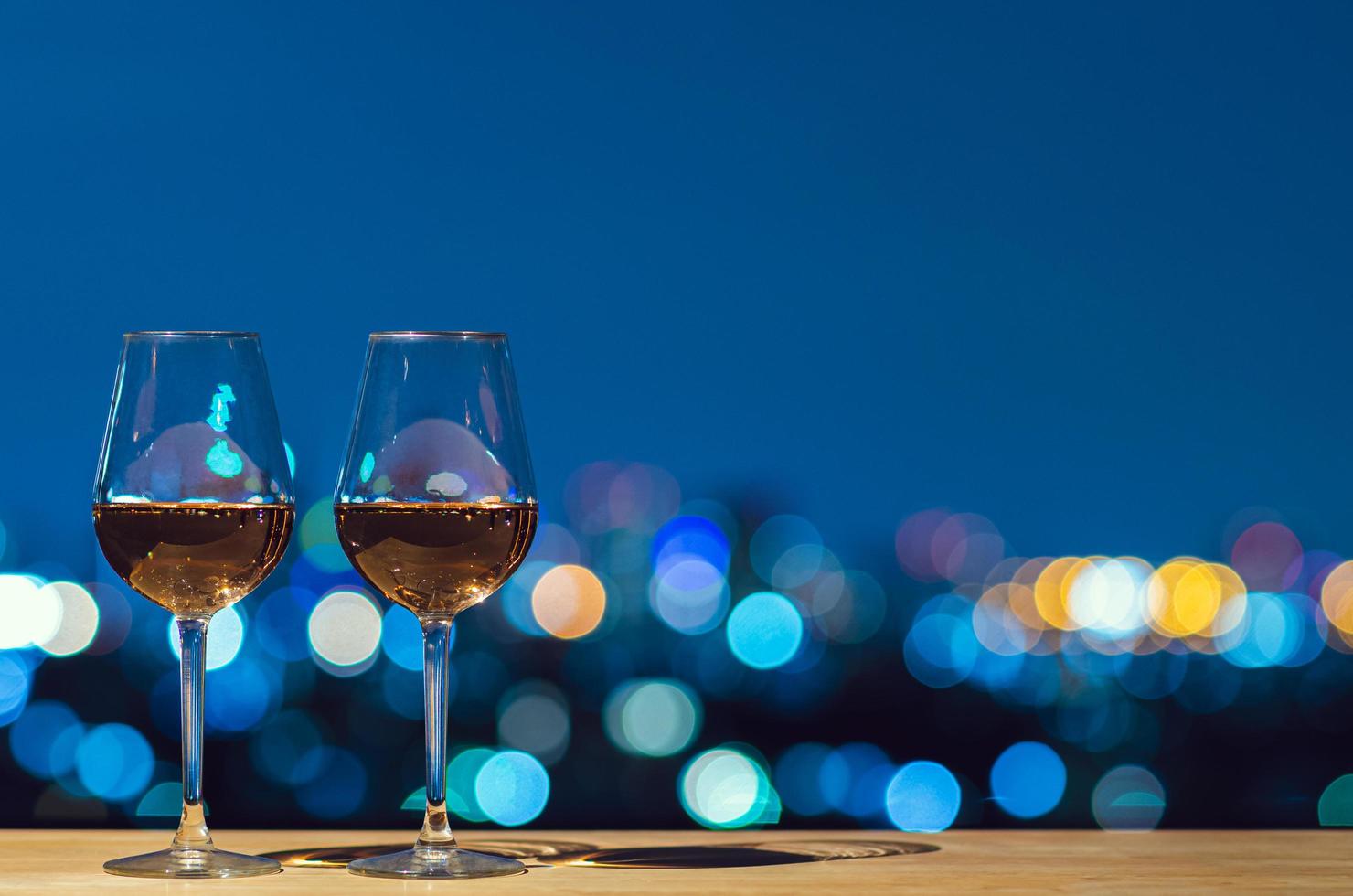 två glasögon av reste sig vin med bokeh stad färgrik ljus från taket byggnad. foto