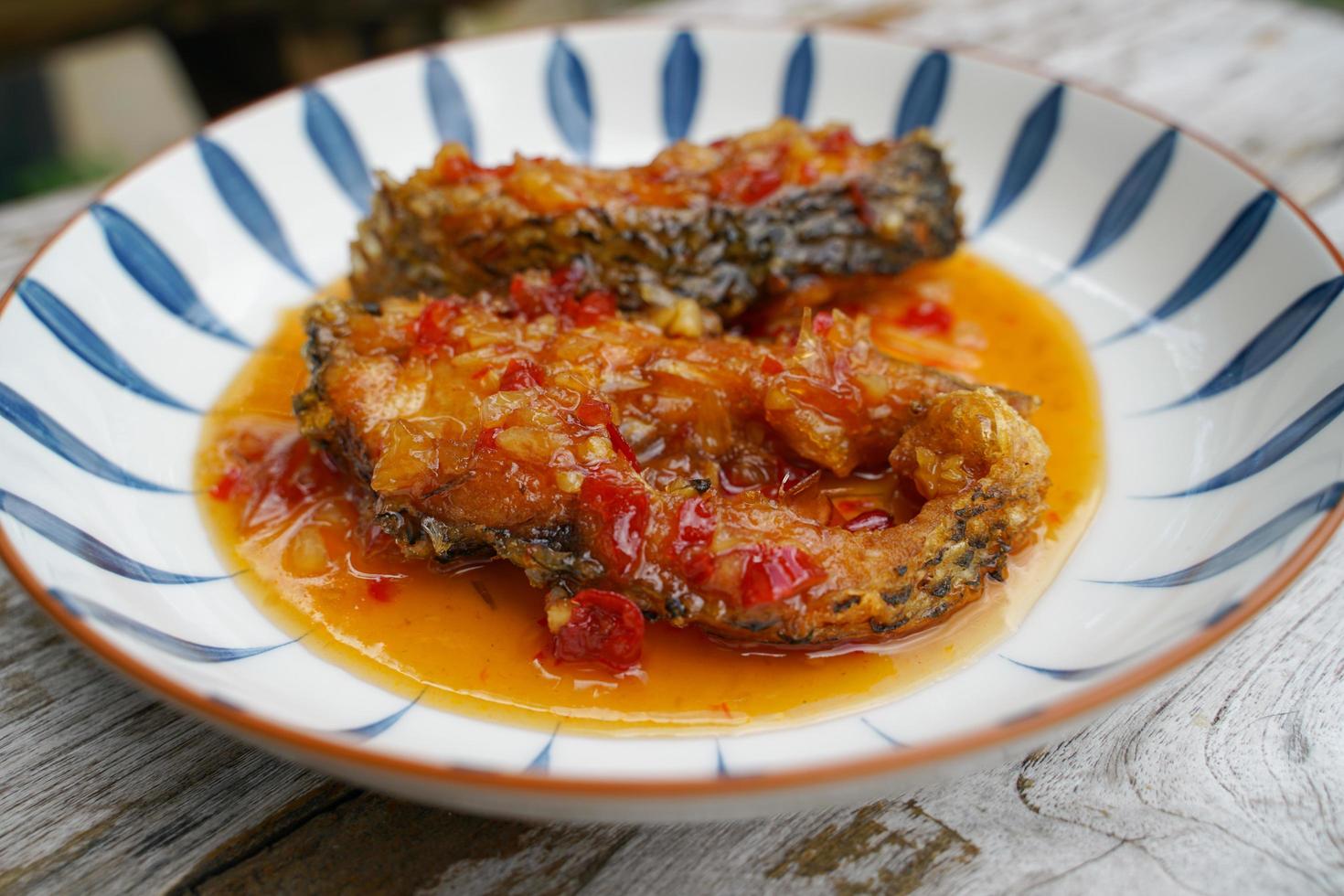 friterad fisk med chili i en keramisk tallrik på ett gammal trä- golv. de smak är sur, ljuv och lite kryddad. foto