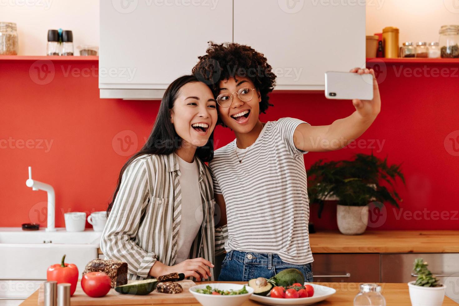 härlig damer i vit blast utgör för selfie medan matlagning vegetabiliska lunch. foto