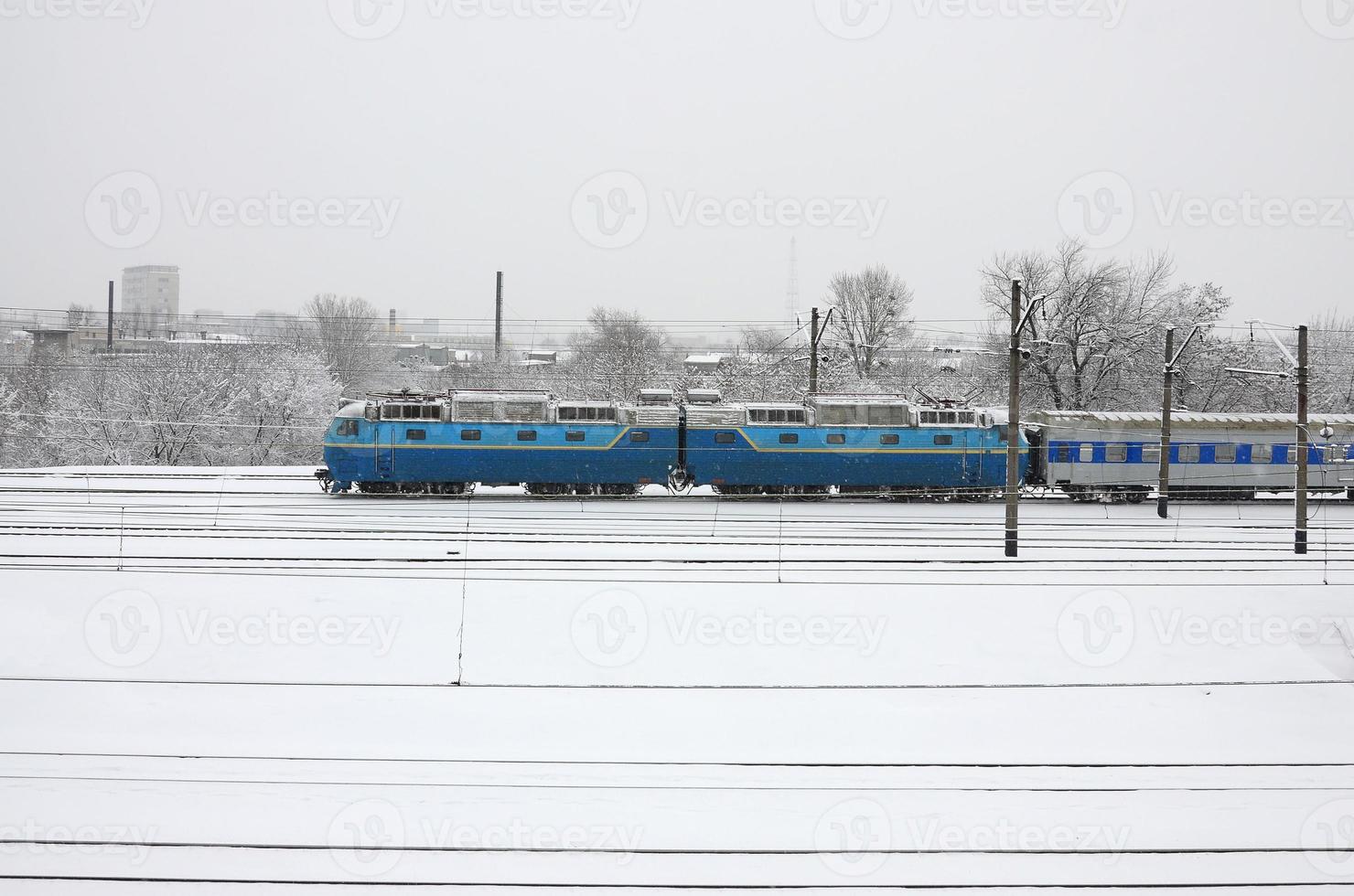 en lång tåg av passagerare bilar är rör på sig längs de järnväg Spår. järnväg landskap i vinter- efter snöfall foto