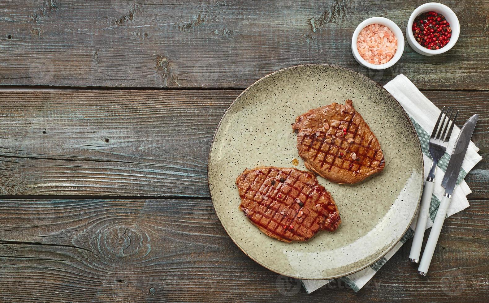 två grillad ribeye biffar, kryddor och tomat-gurka sallad med sur grädde på en trä- tabell. foto