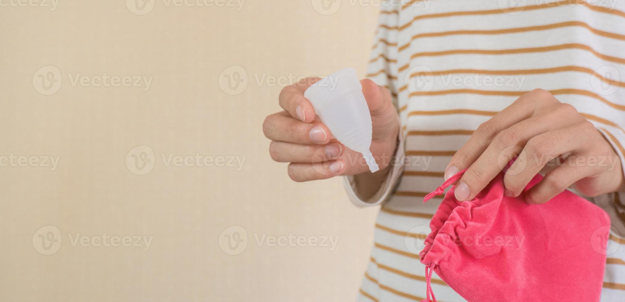 närbild av en ung kvinnas händer i randig pyjamas sätta en menstruations- kopp in i en lagring påse. foto