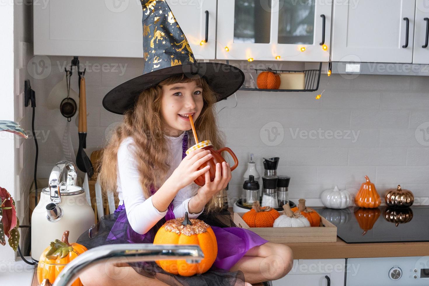 barn drycker pumpa juice, vegetabiliska smoothie eller cocktail från en råna med en sugrör. kök dekorerar för halloween. flicka i en häxa kostym. höst mysigt i Hem foto