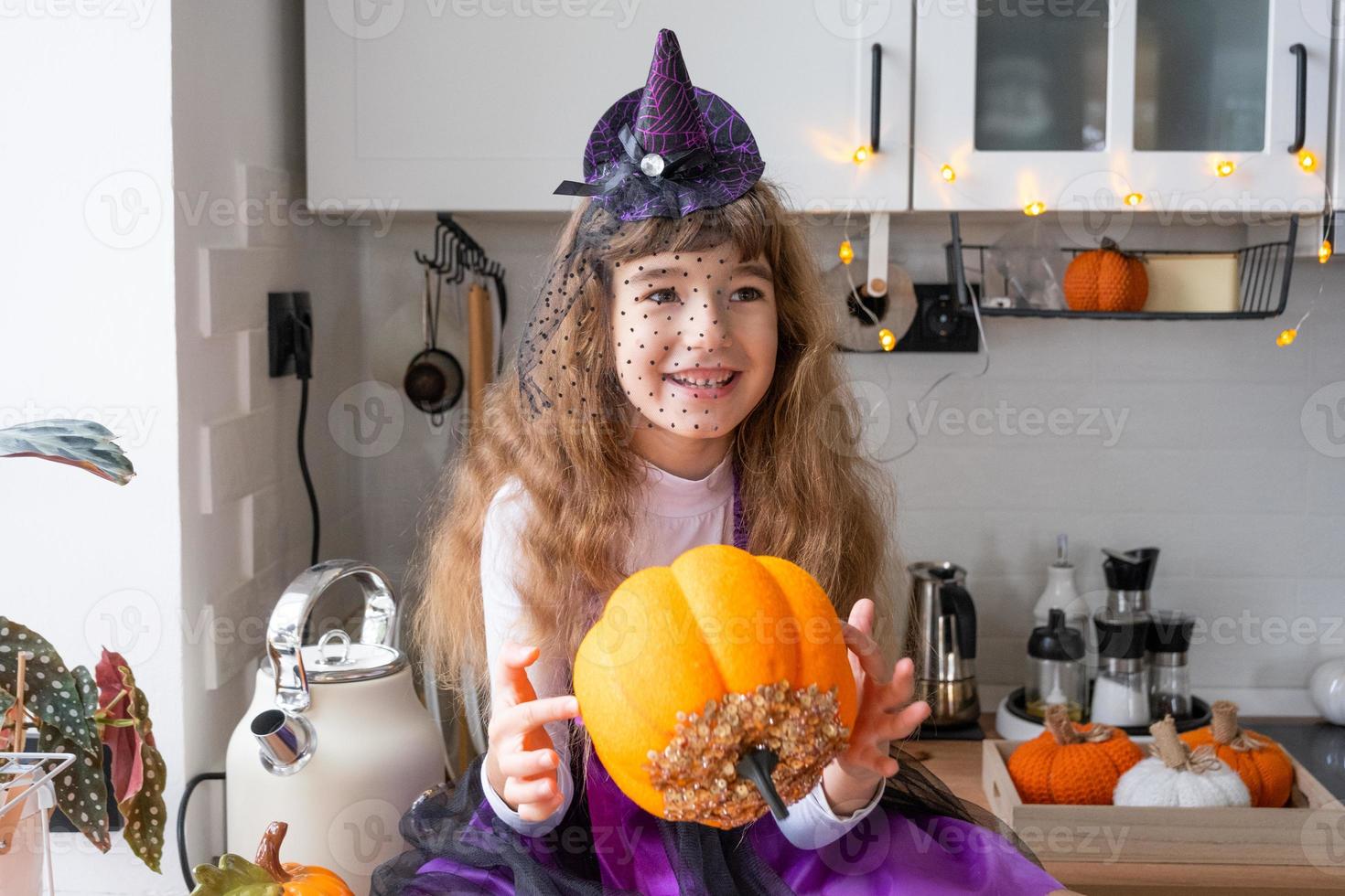 barn dekorerar de kök i Hem för halloween. flicka i en häxa kostym spelar med de dekor för de Semester - fladdermöss, domkraft lykta, pumpor. höst bekvämlighet i hus, scandi-stil kök, loft foto