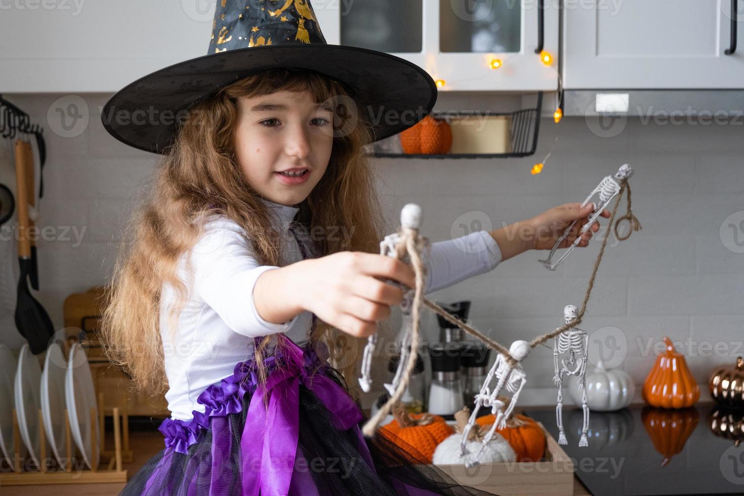 barn dekorerar de kök i Hem för halloween. flicka i en häxa kostym spelar med de dekor för de Semester - fladdermöss, domkraft lykta, pumpor. höst bekvämlighet i hus, scandi-stil kök, loft foto