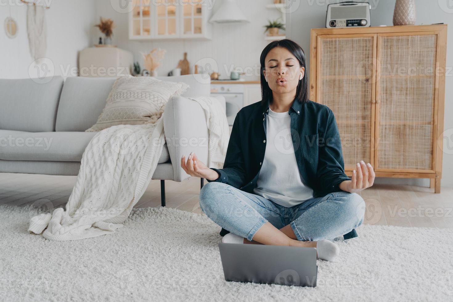 kvinna praxis yoga på bärbar dator, andas djup Sammanträde på golv på Hem. påfrestning lättnad, meditation foto