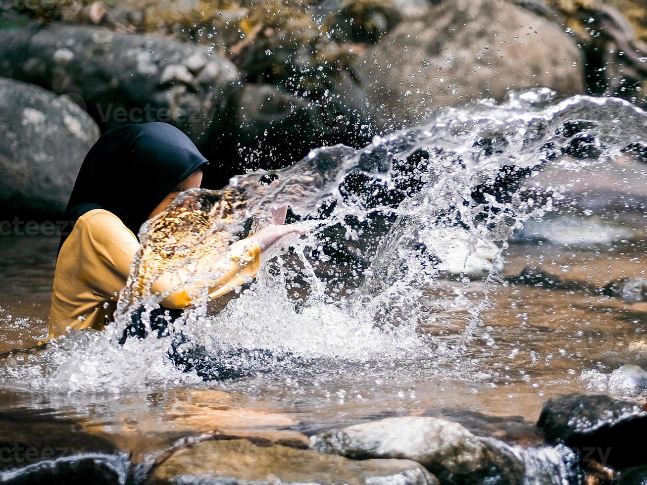 en flicka i hijab är framställning vatten stänk i de regnskog ström foto