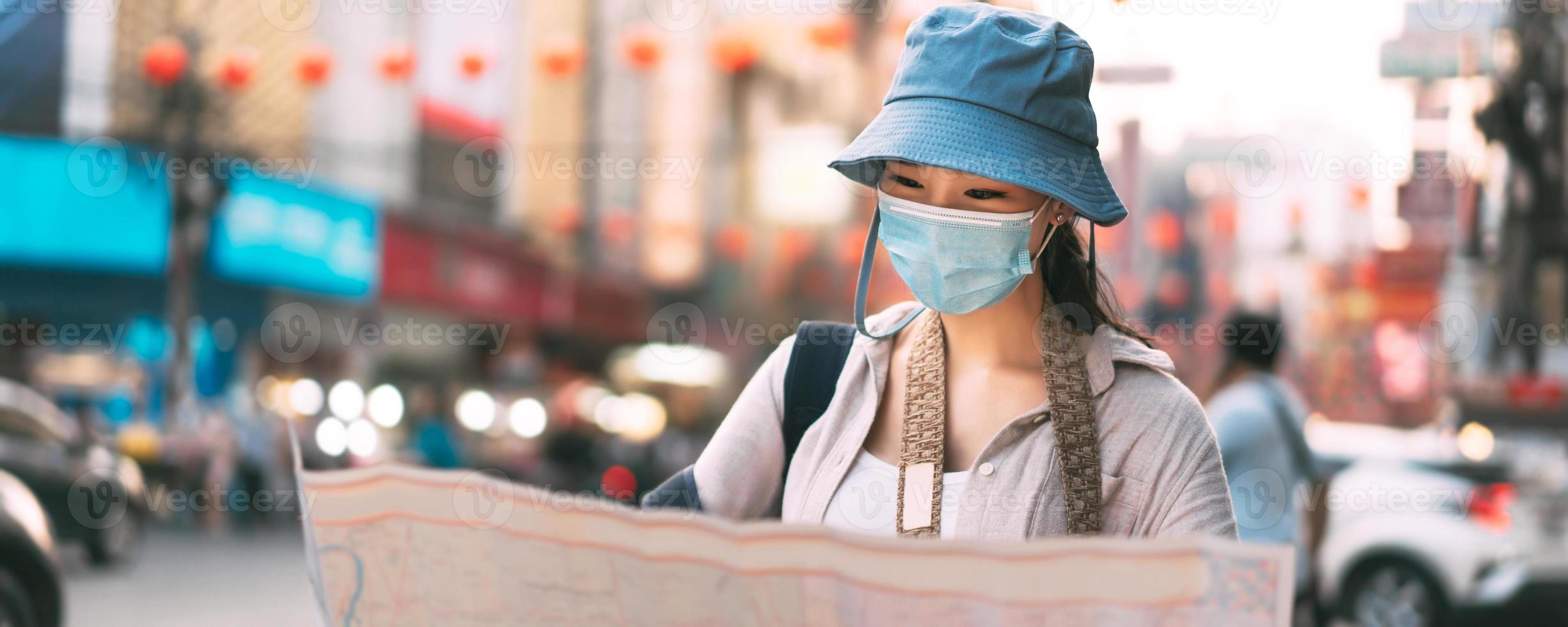 attraktiv ung vuxen resande asiatisk kvinna ha på sig ansikte mask använder sig av Karta baner bakgrund. foto