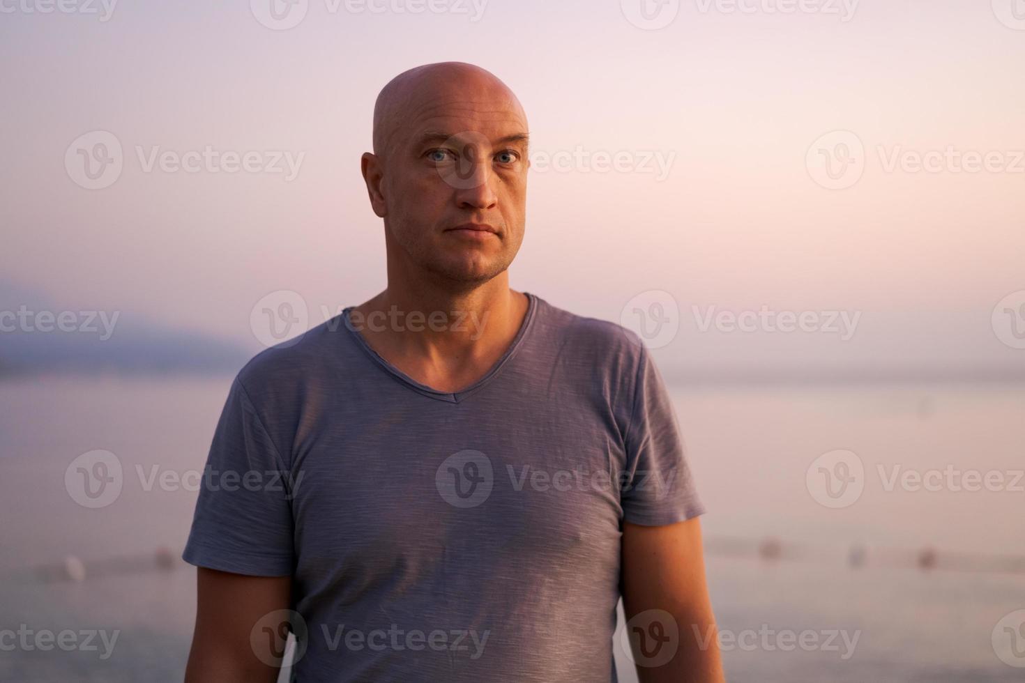 skallig man stående på strand och ser på Fantastisk solnedgång och hav med lugna foto