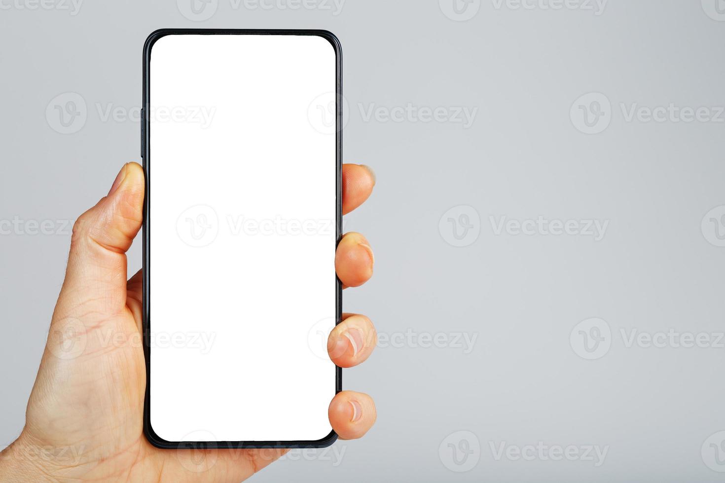 hand innehar svart smartphone med tom vit skärm och modern ramlösa design isolerat på grå bakgrund. foto
