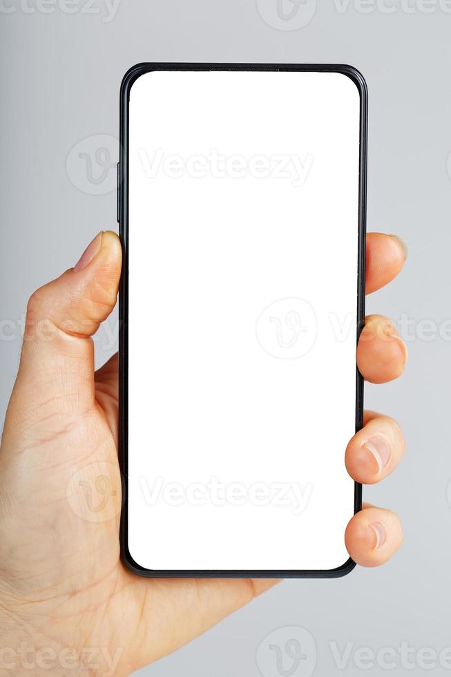 hand innehar svart smartphone med tom vit skärm och modern ramlösa design isolerat på grå bakgrund. foto