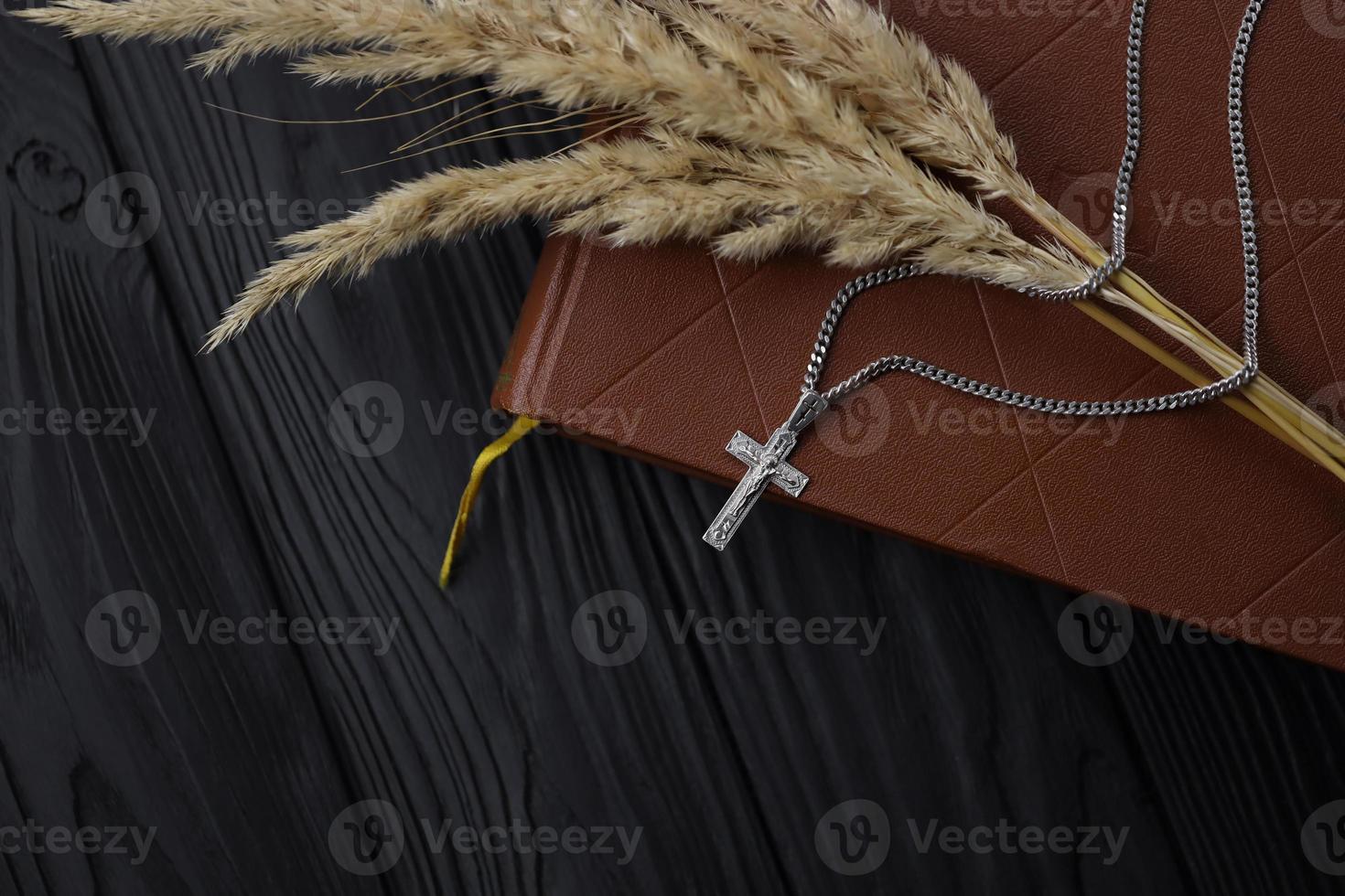 silver- halsband med krucifix korsa på kristen helig bibel bok på svart trä- tabell. be välsignelser från Gud med de kraft av helighet foto