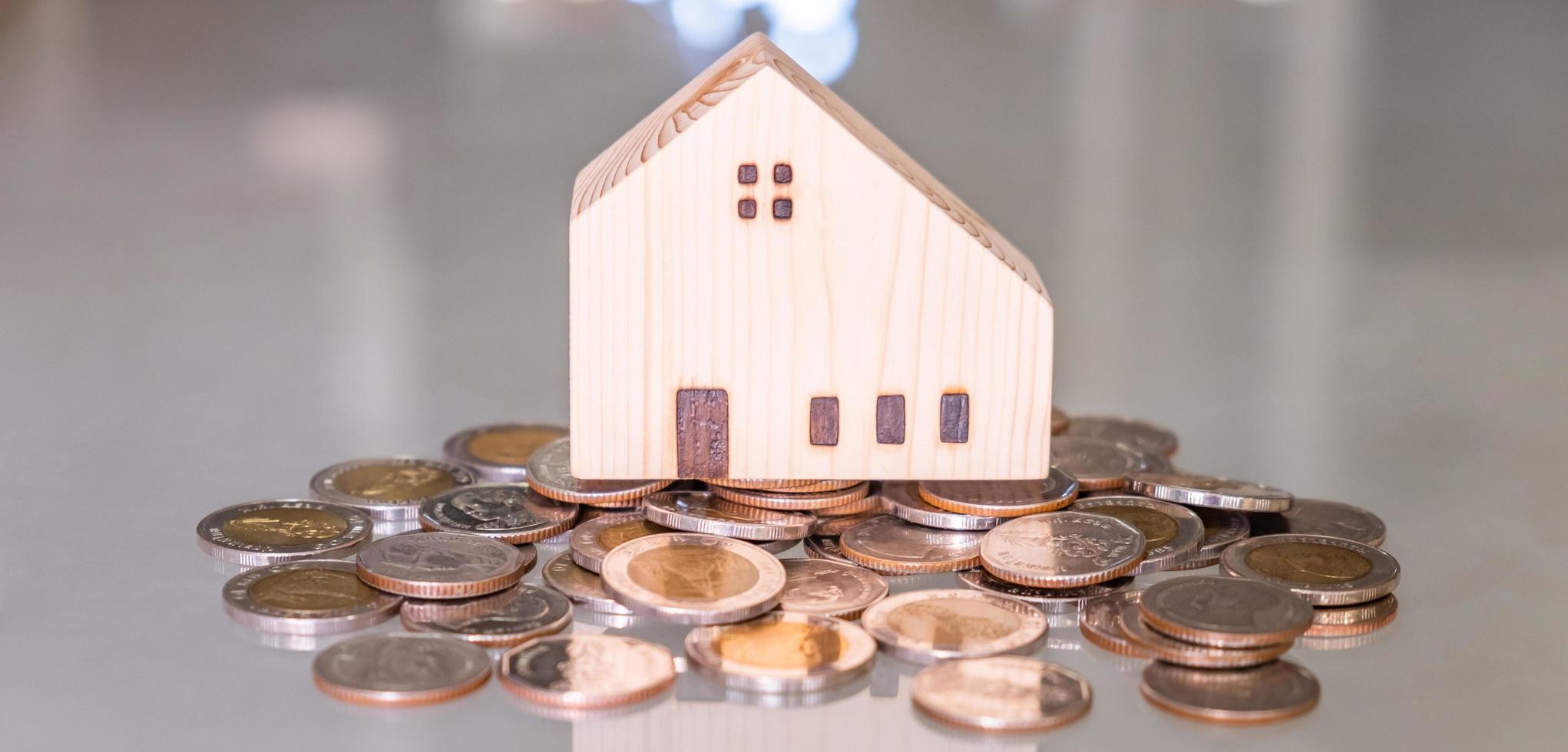 baner skott. selektiv fokus på trä- hus den där sätta på de topp av tillväxt pengar mynt stack på de glas tabell med suddig bakgrund. rikedom och sparande för Hem äganderätt och finansiell begrepp. foto