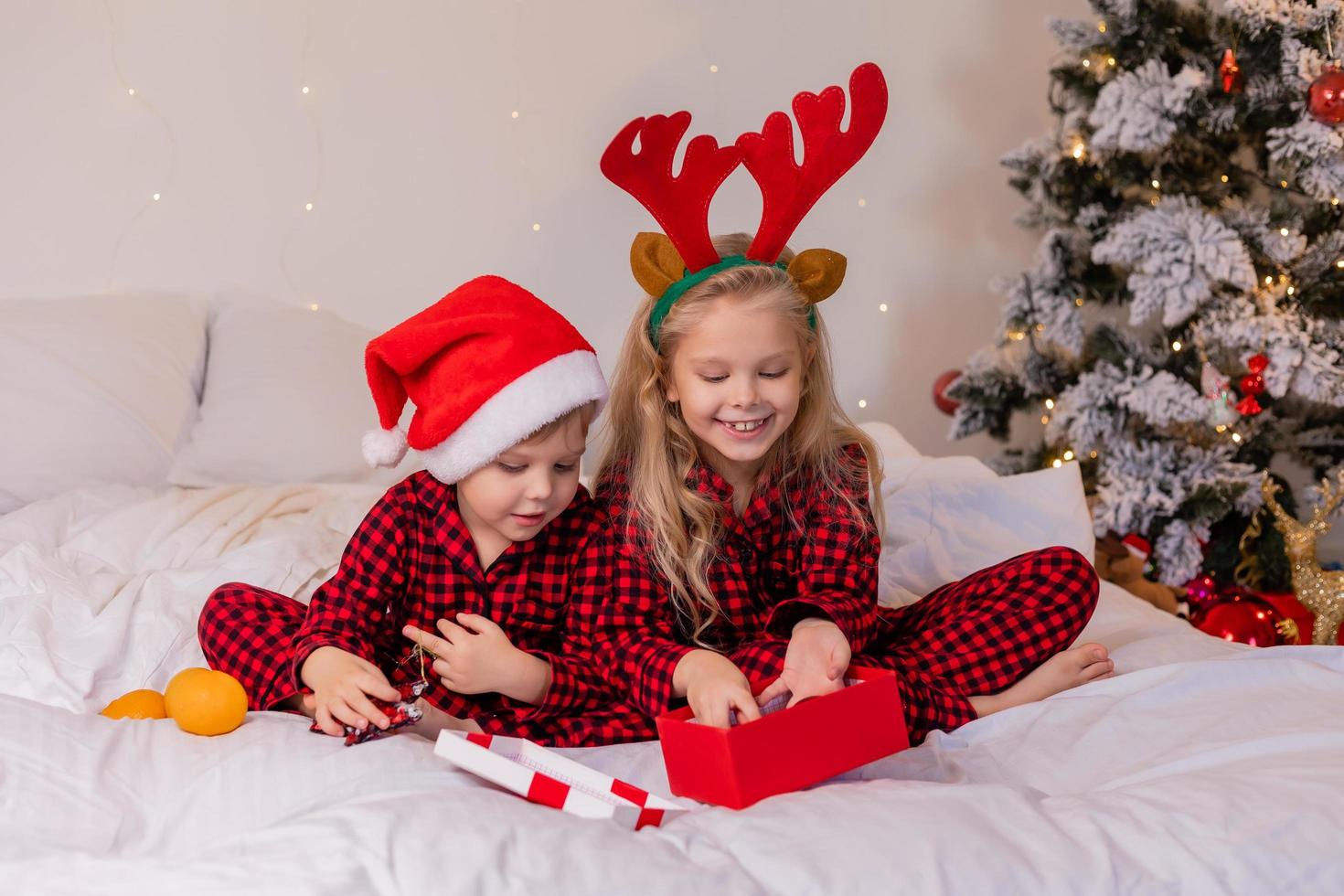 två Lycklig barn i pyjamas för jul är sortering presenterar och spelar med jul leksaker. hög kvalitet Foto