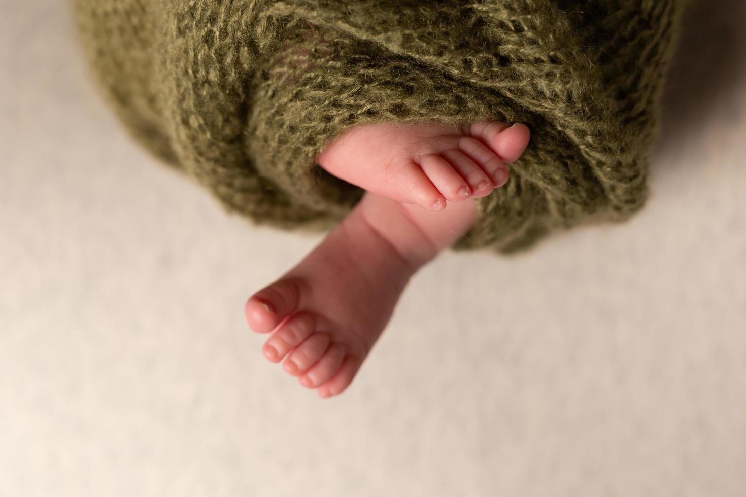 nyfödd bebis fötter på ett gröt bakgrund insvept i en stickat filt foto