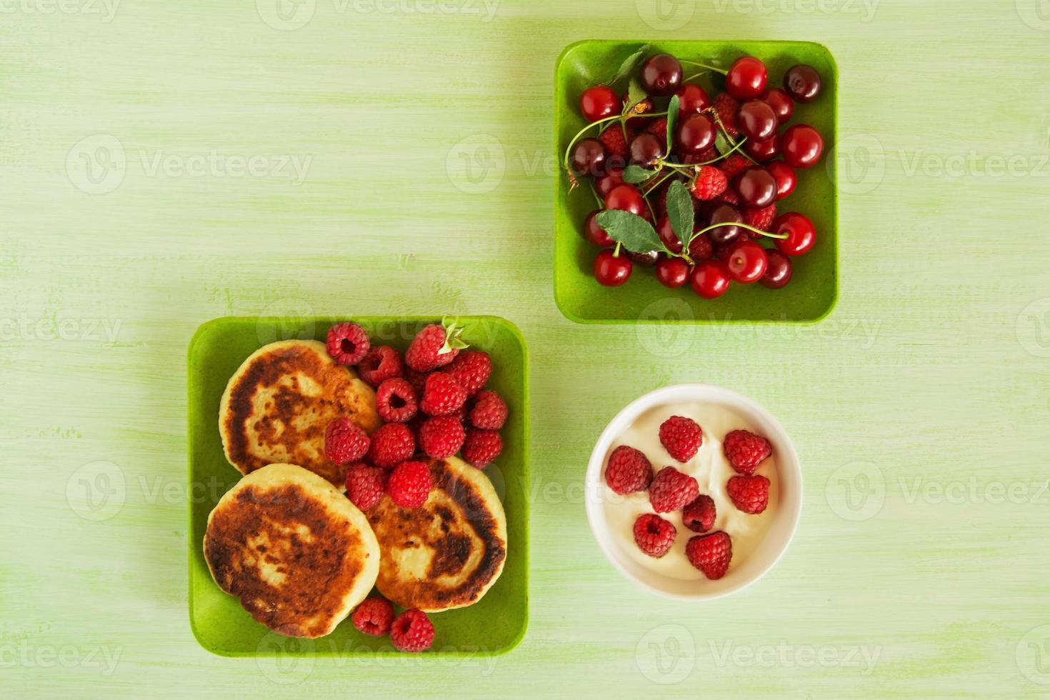 stuga ost pannkakor med färsk hallon, körsbär och sur grädde på de grön plattor på de grön trä- bakgrund, topp se. foto