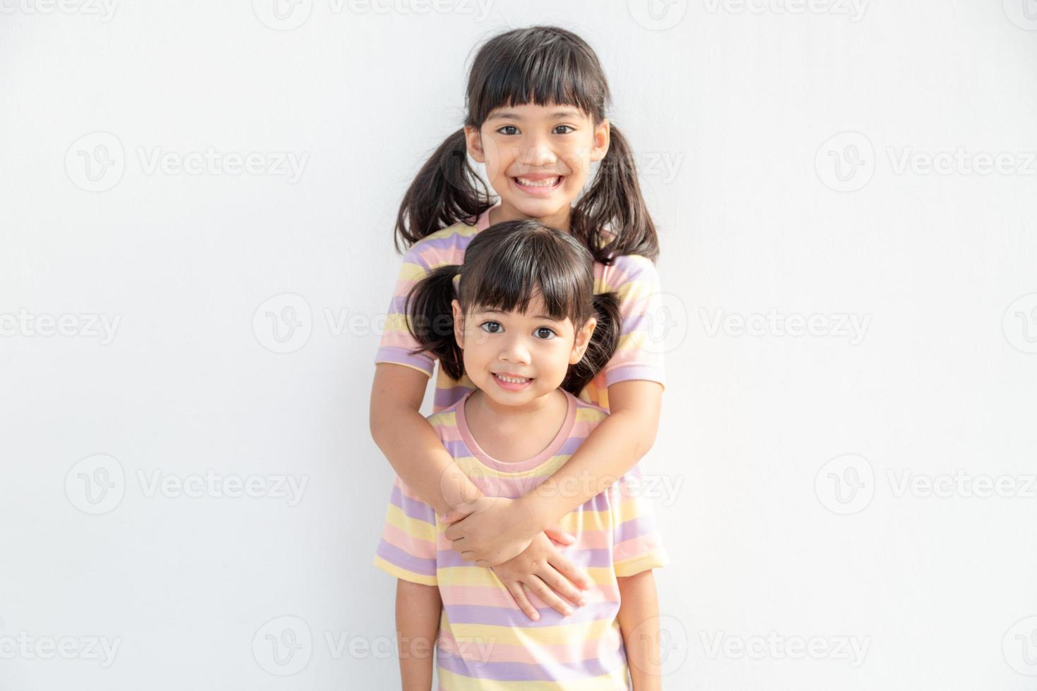 söt Lycklig asiatisk syskon kramas kel känsla kärlek och förbindelse, leende unge flicka syster fattande liten flicka syster på vit bakgrund, 2 barn Bra relationer foto