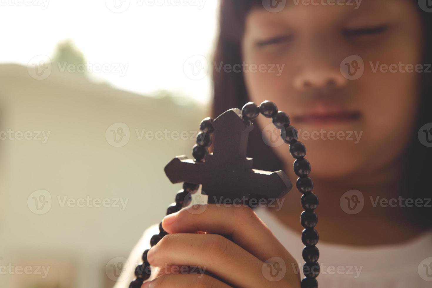 liten asiatisk flicka bön- med innehav de korsa, kristen begrepp. foto