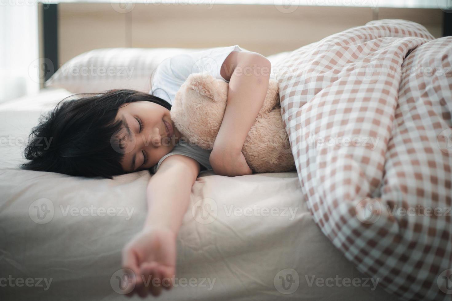 barn liten flicka sover i de säng med en leksak teddy Björn foto